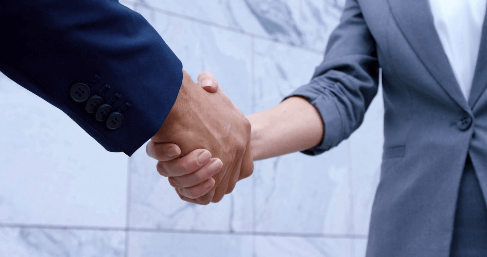 Two people wearing suits exchange a firm handshake
