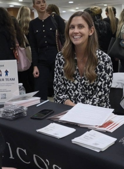 woman with long brown hair, black and white blouse, at a career fair table