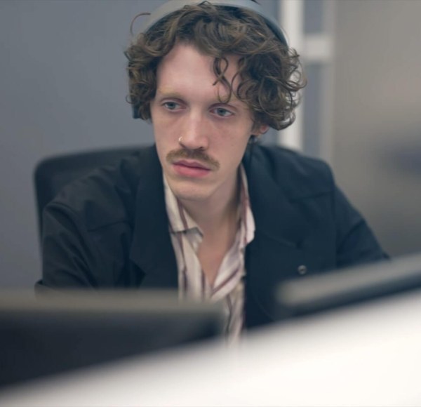 A student in business clothes sits at a desk looking at computer monitors