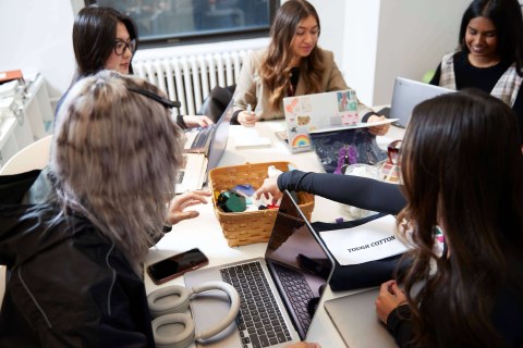 LIM students sit around a table and reach for a basket full of fabric scraps.