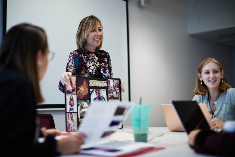 LIM professor Nancy Miller teaches a fashion merchandising course and displays a poster with different designs 