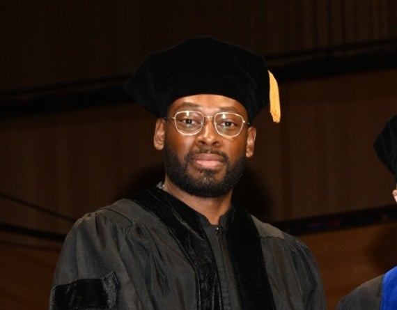 Man wearing glasses in graduation cap-and-gown onstage, holding star-shaped award