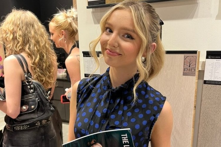 young woman, blond hair, blue and black polka dot blouse, holds magazine
